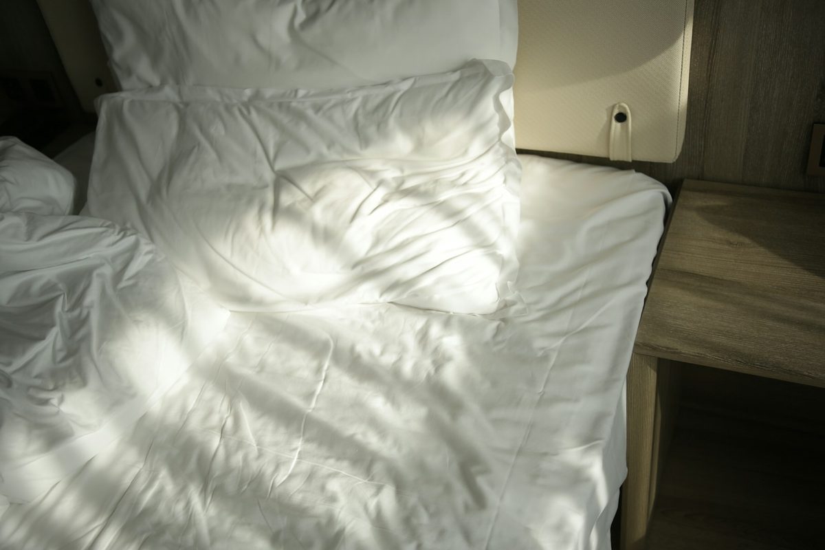 For 1 Hotel Toronto: Close-up of a rumpled white bed with pillows, striped by sun and shadow from a window