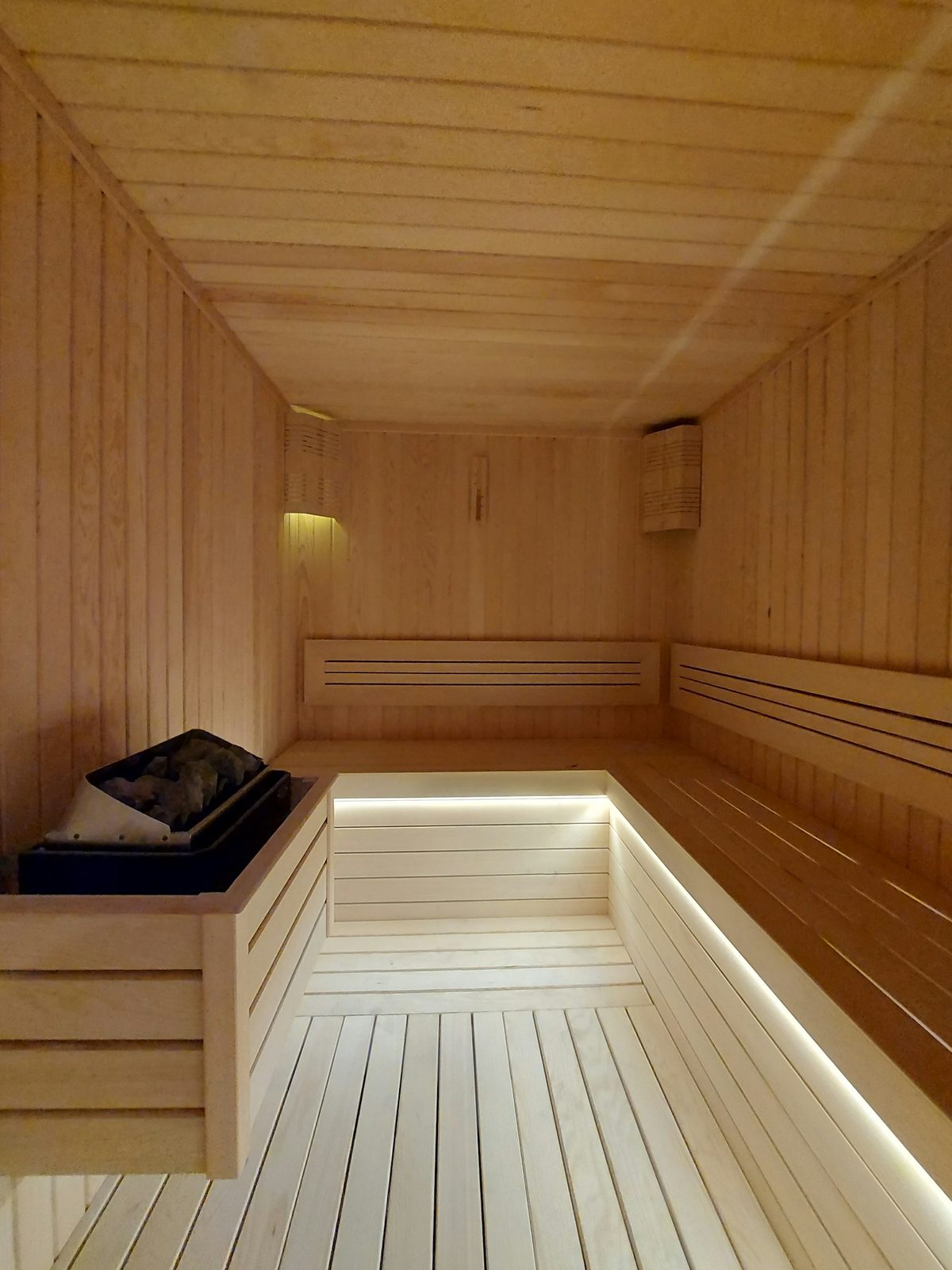 For Alter: An empty pale-wood sauna with bench lighting and a single folded towel, lots of clean space
