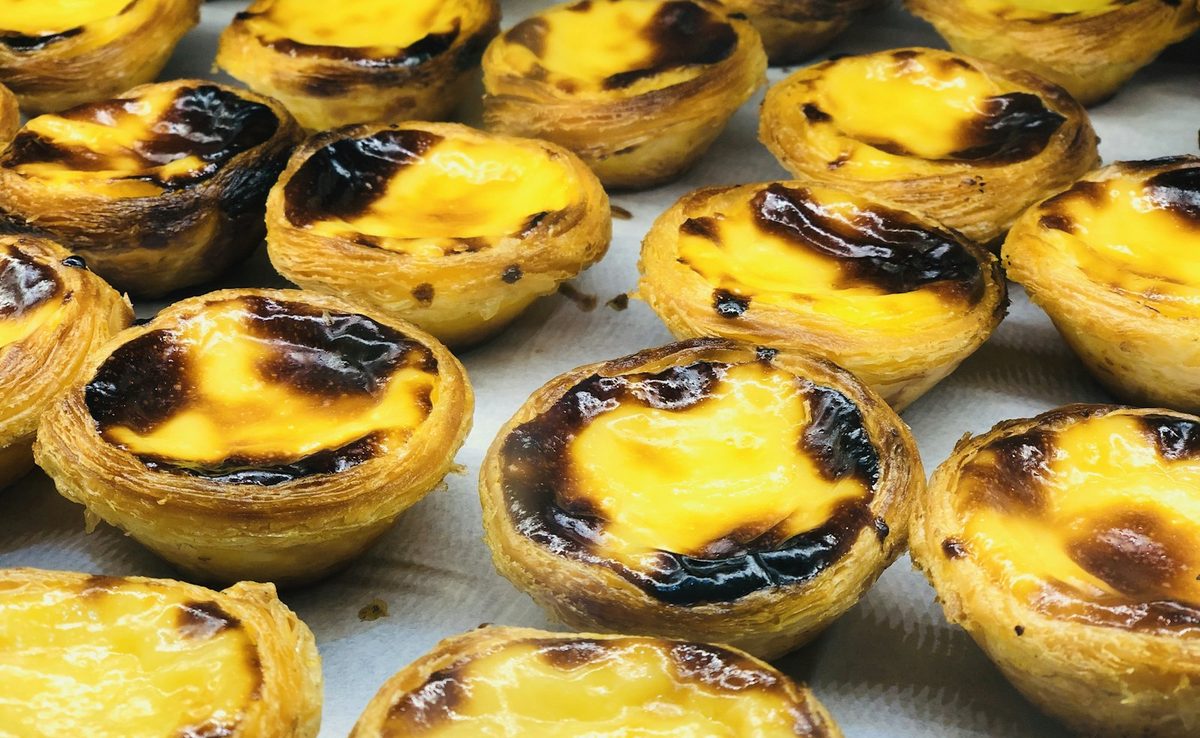 For Café Belém: A close tray of freshly baked pastéis de nata with blistered, caramelised tops, shot in Lisbon.