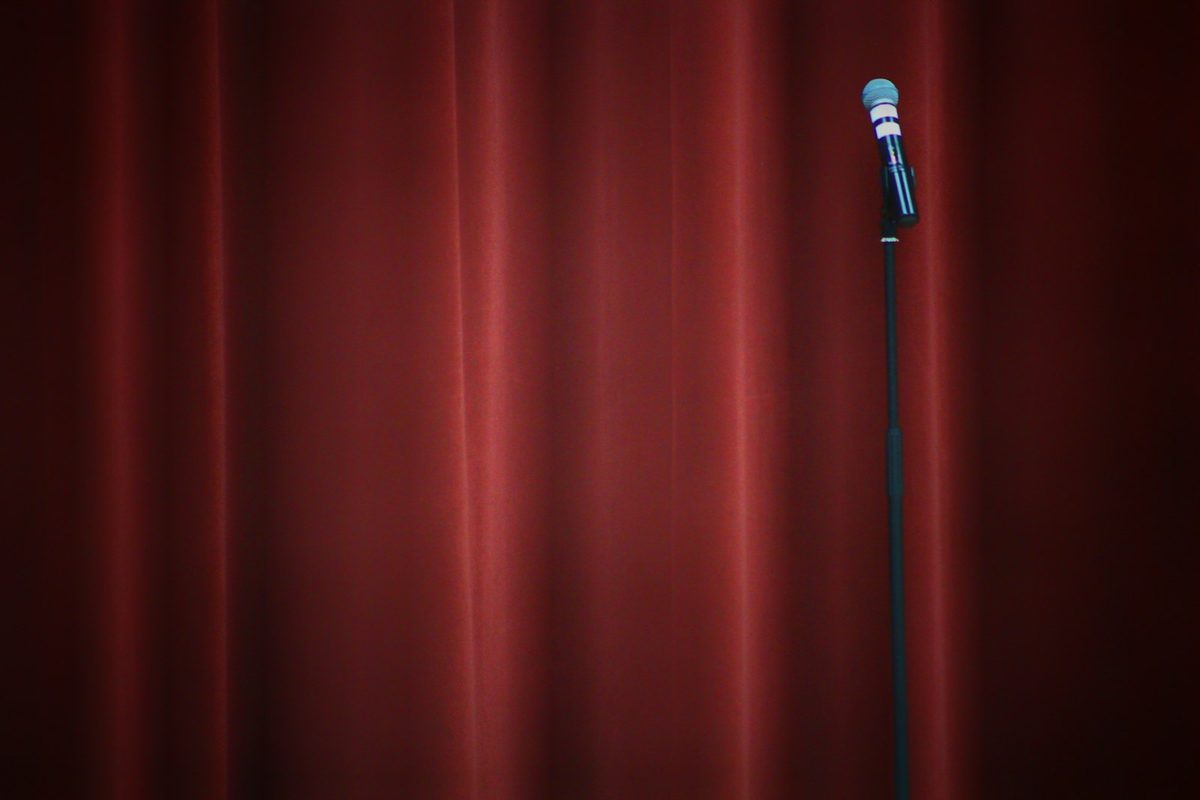 For Comedy Bar: A microphone on a stand in front of a deep red stage curtain
