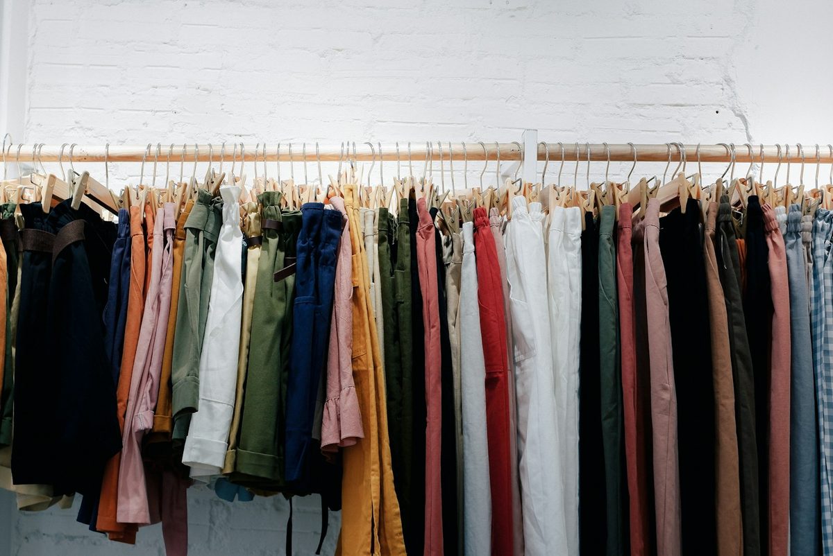 For Courage My Love: A long rail of clothes in muted and bright colours against a white brick wall.