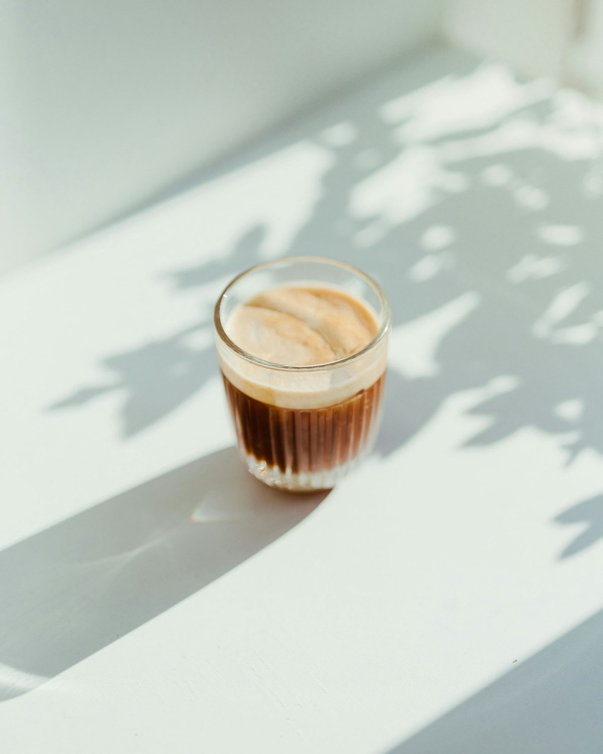 For Doc's Green Door Lounge: A small glass of espresso with crema on a white surface in bright sun and leaf shadows
