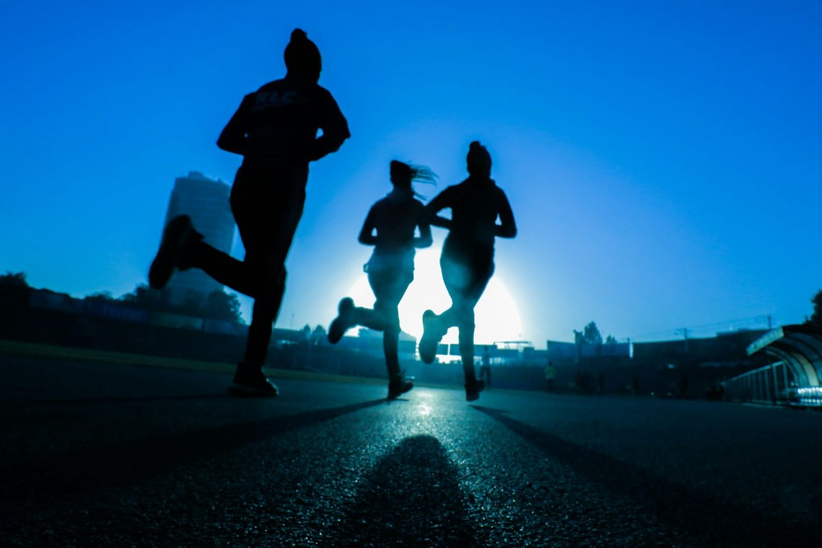 For Frontrunners Toronto: Three runners in silhouette on a road against a deep blue sky with the sun low behind them