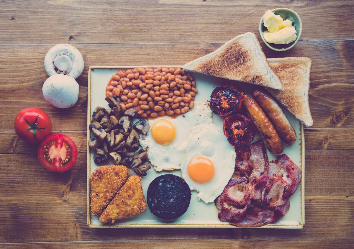 For George Street Diner: Overhead of a full Irish-style breakfast on a tray: fried eggs, beans, sausages, rashers, black pudding, mushrooms and toast on a wooden table