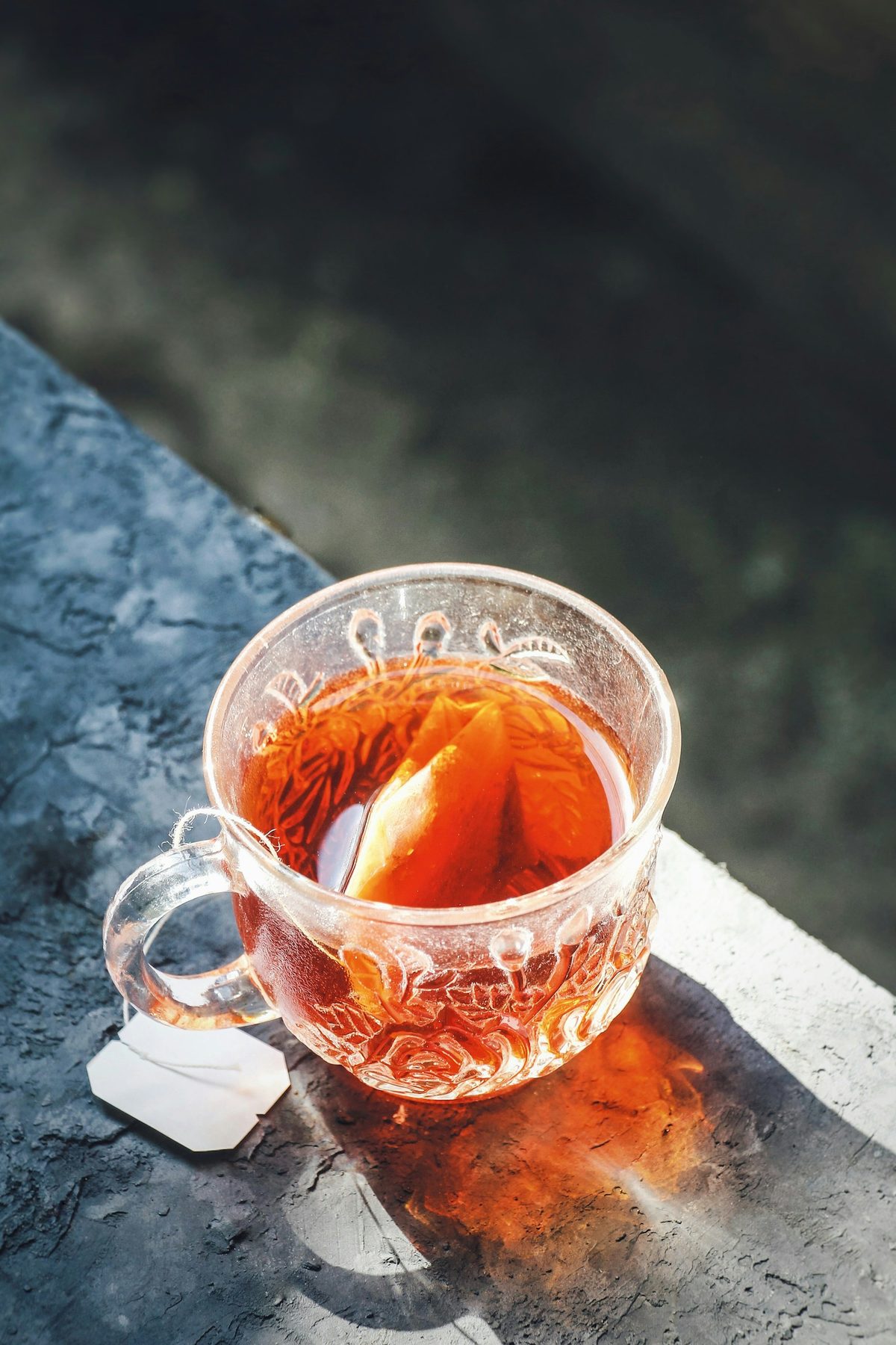For HEYTEA Lab: A glass cup of amber tea in low sunlight on a dark stone ledge, casting an orange glow