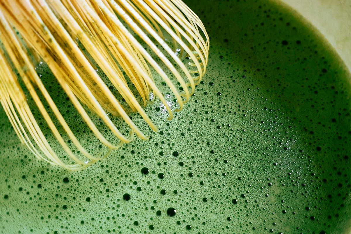 For Matcha Matcha Club: A close-up of a bamboo whisk frothing bright green matcha in a bowl.