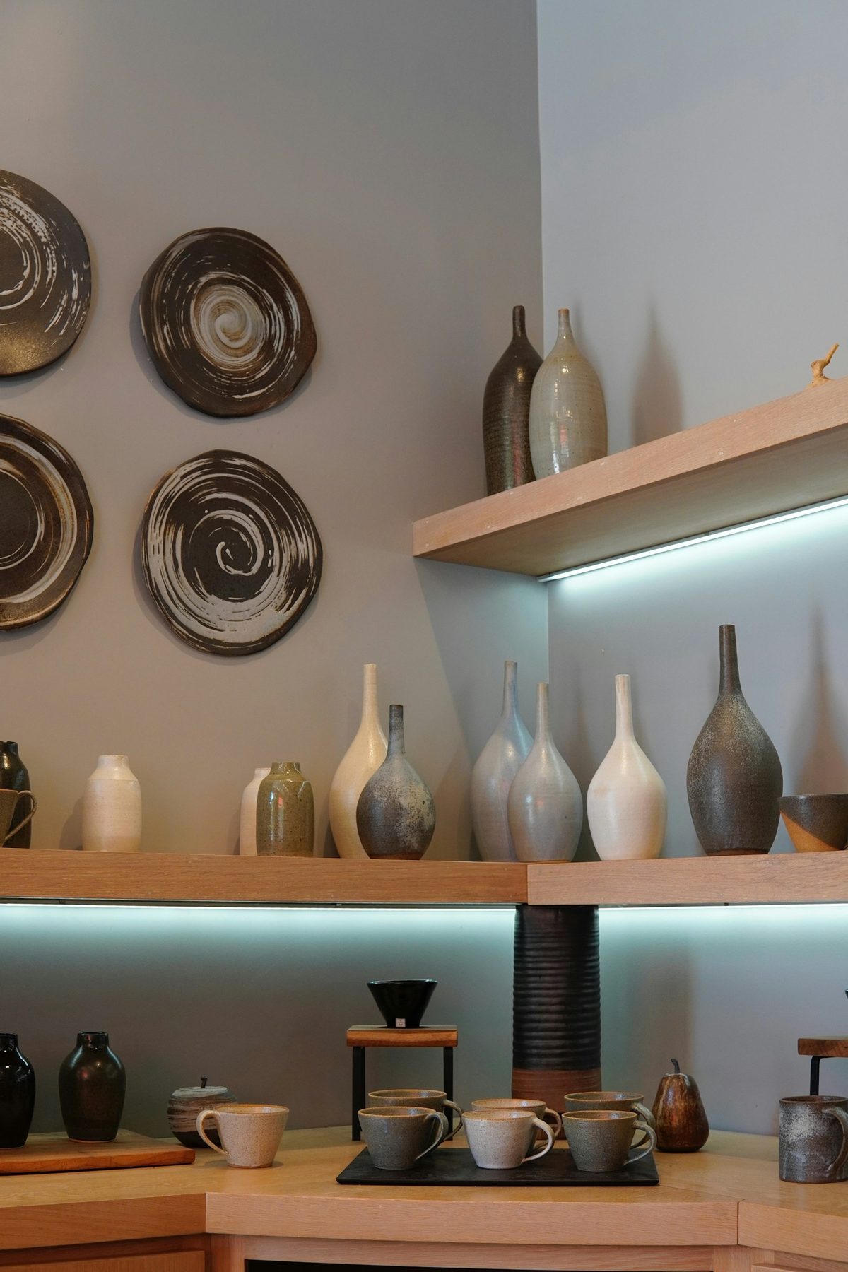 For Mjölk: Handmade vases and plates on floating shelves in a minimal white room (portrait).