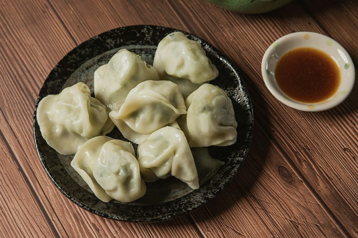 For Mother's Dumplings: A dark plate of boiled jiaozi with a dish of soy dipping sauce on warm wood