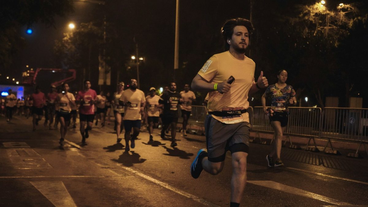 For Parkdale Roadrunners: A pack of runners on a city street at night under warm streetlights, one in front with a race belt