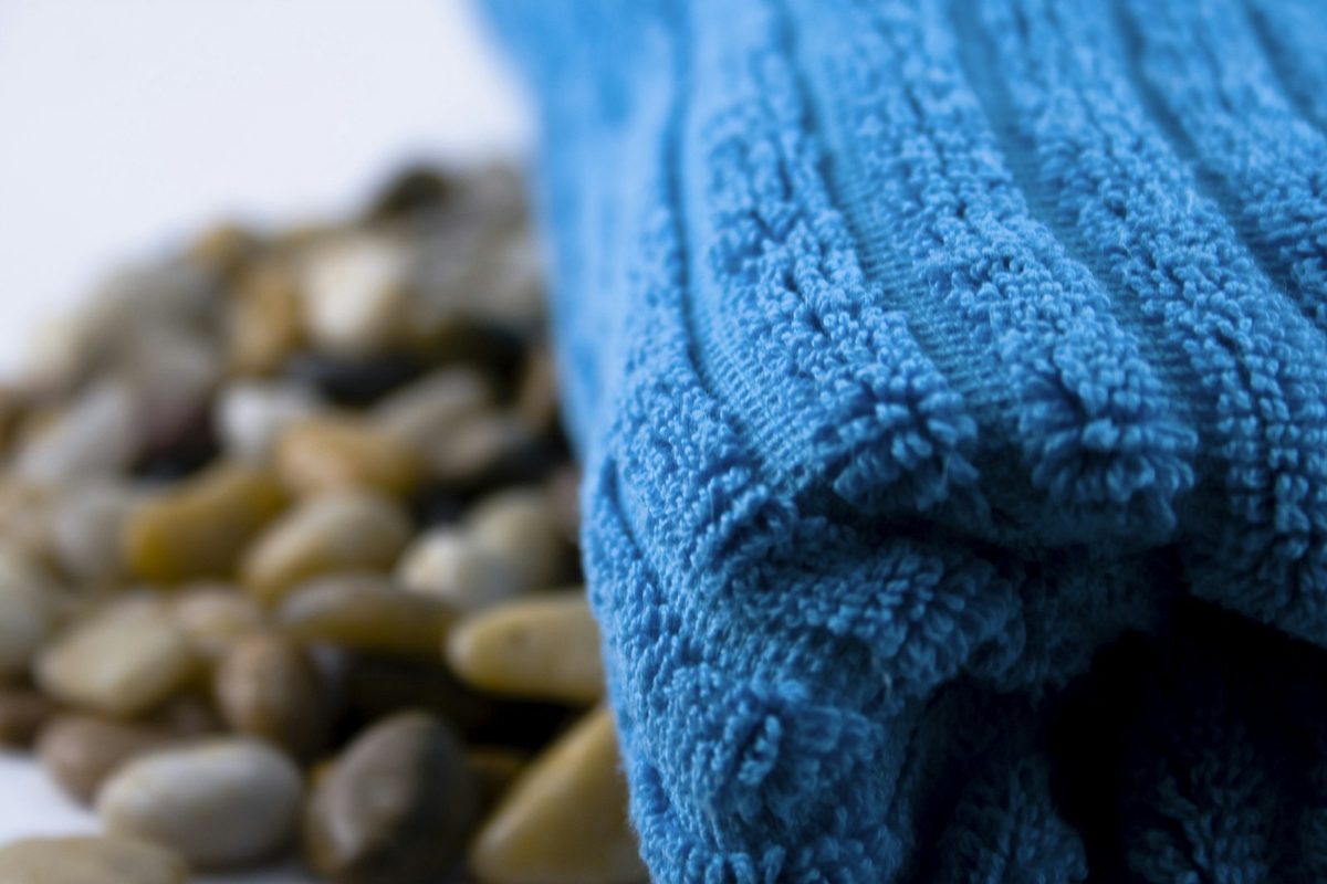 For Sweetgrass Spa: A blue cotton towel folded on smooth grey pebbles, soft focus